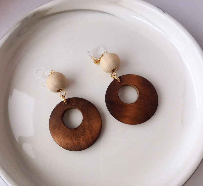 May include: A pair of wooden earrings with a brown circle design and a white wooden bead on each earring.