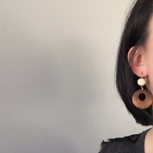 May include: A pair of wooden earrings with a brown and black circle and a white bead.