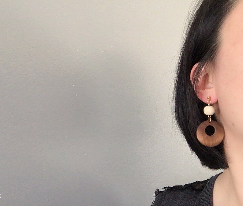 May include: A pair of wooden earrings with a brown and black circle and a white bead.
