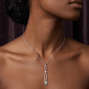 Peut inclure: Collier pendentif argenté avec une chaîne délicate et un design vertical. Le pendentif comprend un ovale, une petite gemme ronde, un autre ovale et une petite médaille plate ronde de 8 mm x 12 mm.