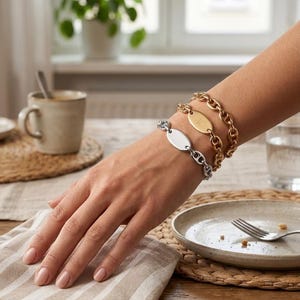 May include: A set of two chain link bracelets, one in a silver tone and one in a gold tone, each featuring a smooth, oval-shaped central plate. The bracelets are constructed with interlocking oval links and secure with a clasp mechanism.