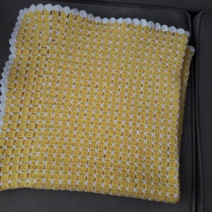 May include: A yellow and white crocheted baby blanket with a scalloped edge.