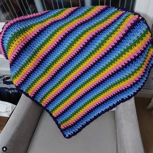 May include: A colorful striped crocheted blanket in shades of blue, green, yellow, and pink. The blanket is folded and draped over a gray armchair.