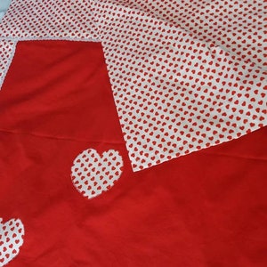 May include: Red bedding with a white heart pattern. The bedding has a white border and three large white hearts with a red heart pattern on a red background.