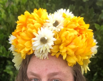 May include: A woman wearing a yellow and white flower crown. The crown is made of silk flowers and is worn on her head.