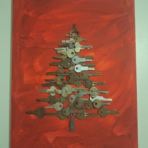 May include: A Christmas tree made of various metal keys arranged on a red painted canvas. The keys are in shades of silver, bronze, and brass, creating a unique holiday decoration. The background is a textured red with brush strokes.