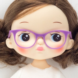 May include: A doll with brown hair wearing purple glasses and a white shirt.