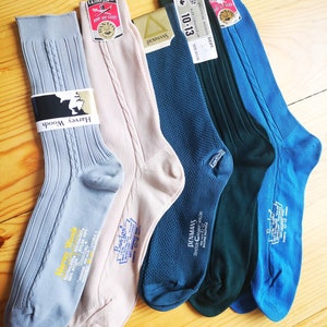 Puede incluir: Seis pares de calcetines de varios colores, incluyendo azul, verde y rosa. Los calcetines están hechos de nylon y tienen diferentes etiquetas de marca, incluyendo Harvey Woods, Banlon y Denmans.