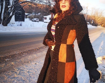 Könnte beinhalten: Eine Frau trägt einen langen, braunen, flauschigen Mantel mit Patchwork-Muster. Der Mantel hat eine braune, schwarze und orangefarbene Farbgebung. Sie trägt eine Sonnenbrille und hat langes, lockiges Haar. Die Frau steht auf einer schneebedeckten Straße.