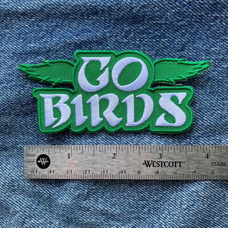 May include: Green and white embroidered patch with the words "GO BIRDS" and a green bird wing on each side. The patch is measured against a ruler.
