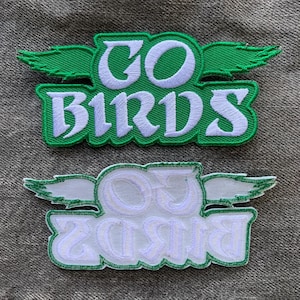 May include: Two green and white embroidered patches with the text "GO BIRDS" in a stylized font. The top patch has green wings and the bottom patch has white wings.