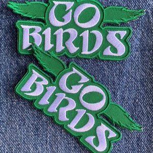 May include: Two green and white embroidered patches with the text "GO BIRDS" in a white cursive font. The patches have a green bird wing design.