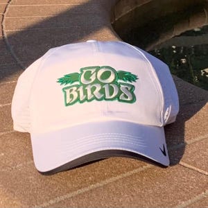 May include: White baseball cap with a green and white embroidered logo that says "GO BIRDS".