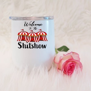 May include: White stainless steel tumbler with a black and red design. The design features three red and white striped circus tents with the text "Welcome to the Shitshow".