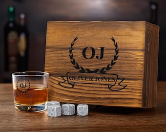May include: A wooden box with a personalized engraved design featuring the initials "OJ" and the name "Oliver Jones" in a banner. The box contains a whiskey glass and four gray whiskey stones.