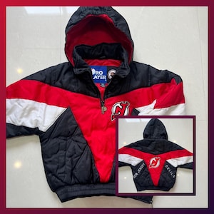 May include: Black, red, and white Pro Player jacket with a hood. The jacket features a New Jersey Devils logo on the front and back. The jacket has a zip closure and a quilted design.