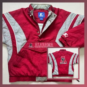 May include: Red and gray Starter jacket with "ALABAMA" printed across the chest. The jacket features a half-zip closure, a small pocket, and the Starter logo. The back of the jacket has a Crimson Tide logo.