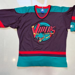 May include: A purple hockey jersey with teal and red accents. The jersey features the word "Vipers" in red and yellow, along with a teal snake logo. The jersey has a V-neck and is made by Starter.