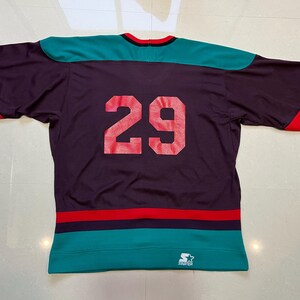 May include: Purple hockey jersey with teal and red accents. The number 29 is printed in red on the back. The jersey has a teal collar and sleeves with red stripes. A Starter logo is visible at the bottom.