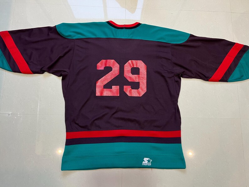 May include: Purple hockey jersey with teal and red accents. The number 29 is printed in red on the back. The jersey has a teal collar and sleeves with red stripes. A Starter logo is visible at the bottom.