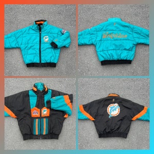 May include: A vintage Miami Dolphins reversible jacket. One side is teal blue with the team logo and "Dolphins" embroidered in gold. The other side is black with a teal blue and orange color block design and a dolphin logo.