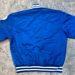 May include: A blue satin bomber jacket with white and navy blue striped ribbing around the collar, cuffs, and hem.