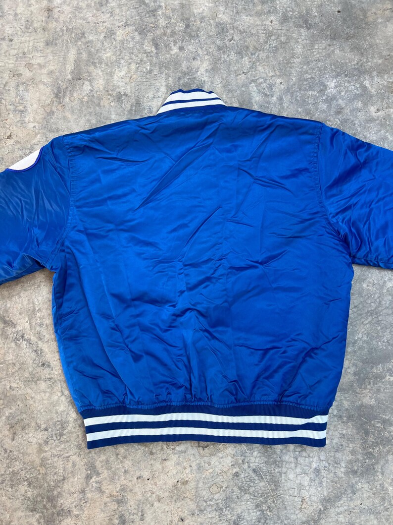 May include: A blue satin bomber jacket with white and navy blue striped ribbing around the collar, cuffs, and hem.