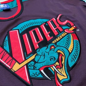 May include: A purple mesh jersey featuring a large embroidered logo of a snake and the word "Vipers" in red and white. The jersey has teal and red accents on the collar and sleeves. The Starter brand tag is visible.