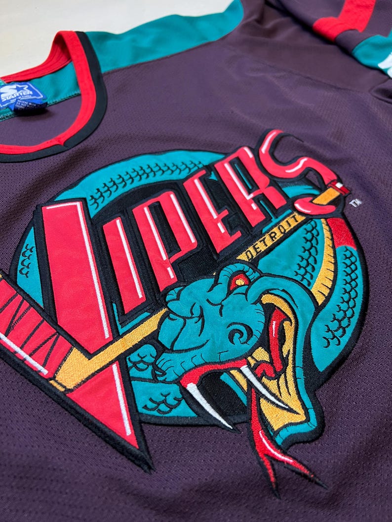 May include: A purple mesh jersey featuring a large embroidered logo of a snake and the word "Vipers" in red and white. The jersey has teal and red accents on the collar and sleeves. The Starter brand tag is visible.