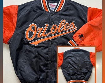 May include: Black and orange Baltimore Orioles satin jacket. The jacket features the team name in orange script across the chest, orange sleeves, and a button-up front. The collar and cuffs have white and orange stripes.