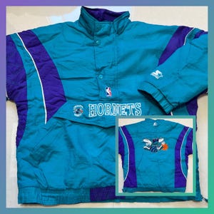 Peut inclure: Veste anorak vintage des Hornets, de couleur teal, violet et blanc. La veste porte le nom de l'équipe "Hornets" sur la poitrine, ainsi que le logo NBA. Une petite image de la veste montre le logo de l'équipe au dos. La veste porte le logo Starter.