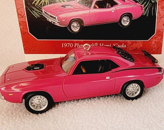 Puede incluir: Un adorno de coche rosa de 1970 Plymouth Hemi 'Cuda. El adorno es una réplica del clásico coche de carreras con rayas negras y un interior detallado.