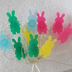Peut inclure: Une guirlande lumineuse avec des ampoules en forme de lapin de différentes couleurs, notamment vert, bleu, rose et jaune.