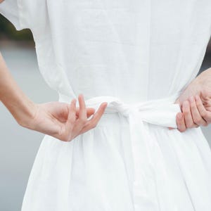 Linen wedding dress in motion, back view against wall