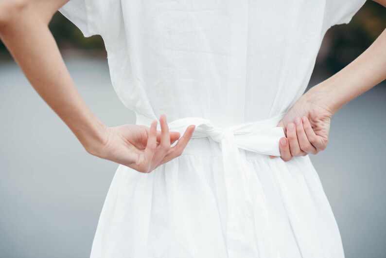 Linen wedding dress in motion, back view against wall