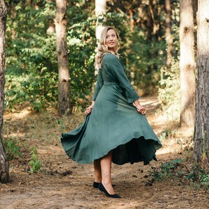 Green long sleeve linen wrap dress twirling in forest, skirt in motion