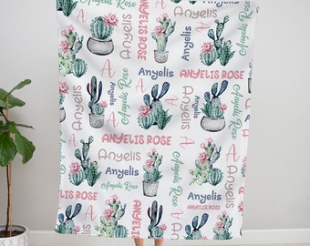 May include: A white baby blanket with a repeating pattern of green and pink cacti and the name "Anyelis Rose" written in pink and green.