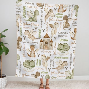 May include: A white baby blanket with a repeating pattern of green and brown dragons, castles, and the names "Yohan" and "Pierre".