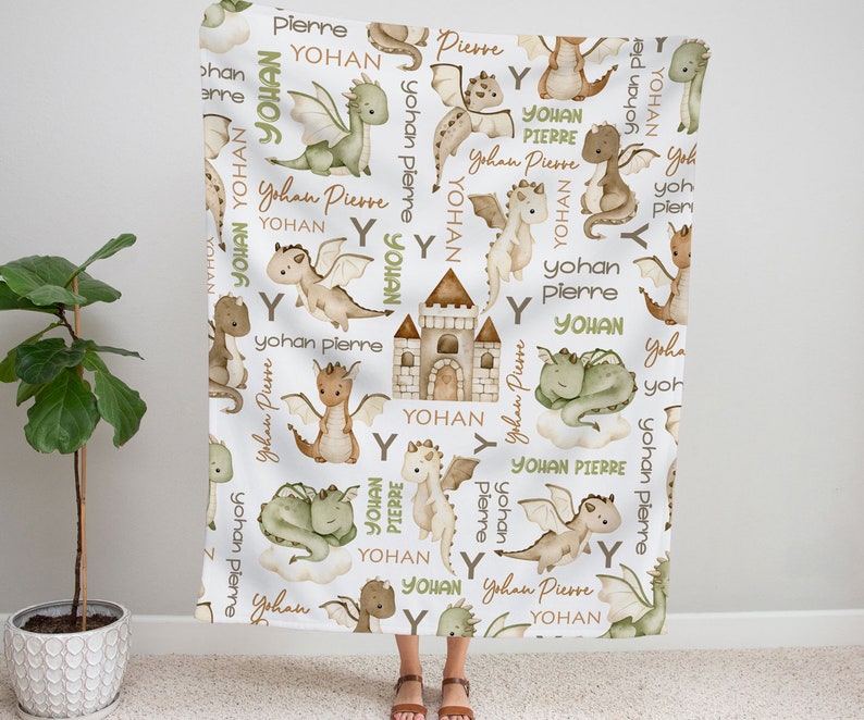 May include: A white baby blanket with a repeating pattern of green and brown dragons, castles, and the names "Yohan" and "Pierre".