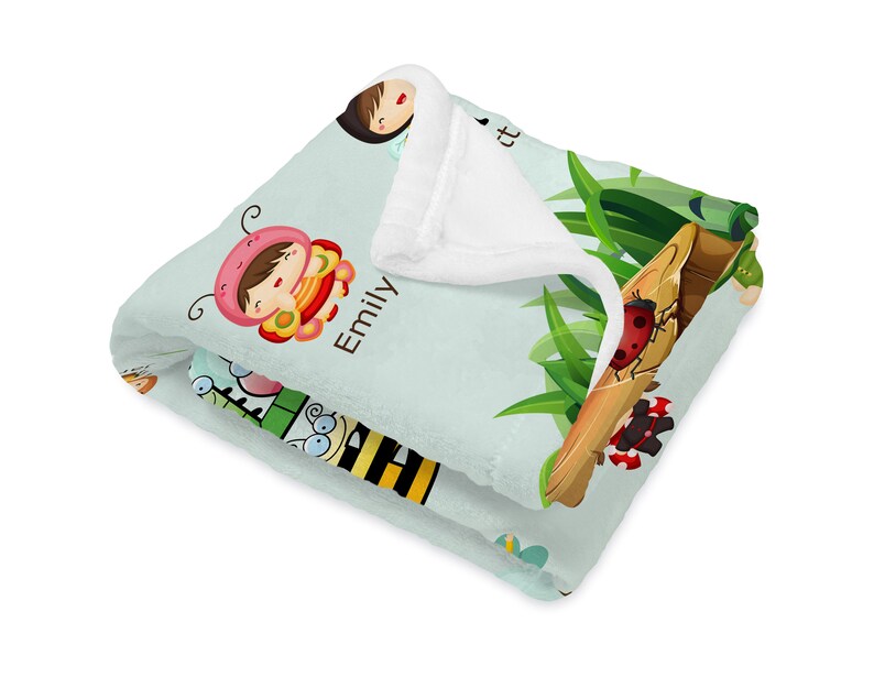 May include: A light blue fleece blanket with a white sherpa lining. The blanket features a whimsical design with a girl dressed as a ladybug, a bee, a ladybug, and a butterfly. The text "Emily" is printed on the blanket.