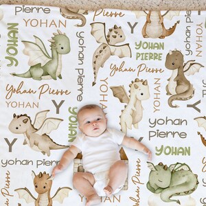 May include: A white baby blanket with a repeating pattern of green and brown dragons and the names "Yohan" and "Pierre".