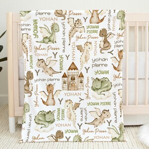 May include: A white baby blanket with a repeating pattern of green and brown dragons, a castle, and the names "Yohan" and "Pierre".