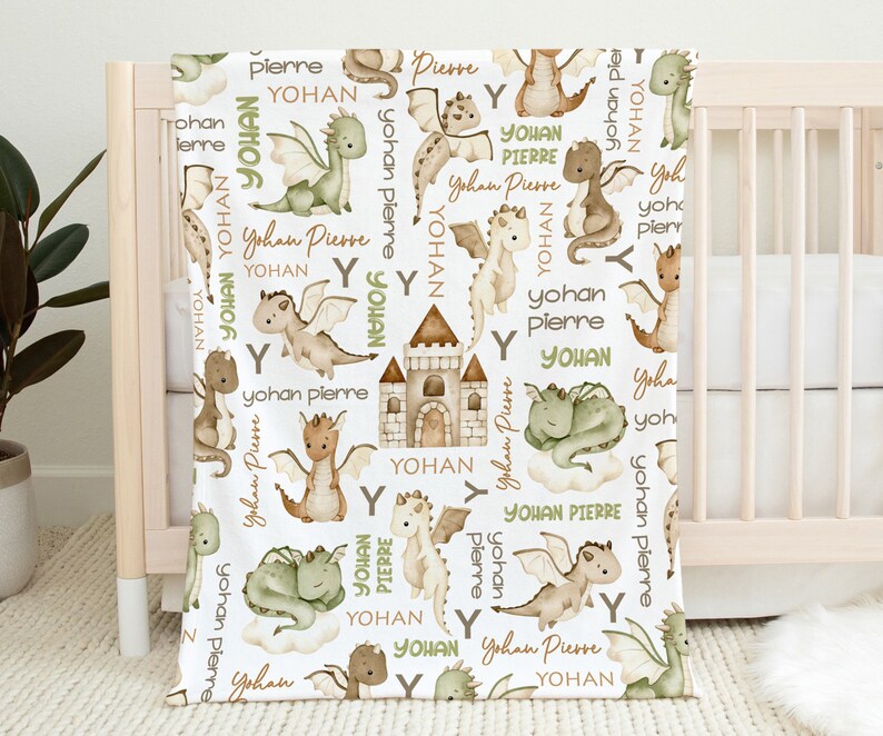 May include: A white baby blanket with a repeating pattern of green and brown dragons, a castle, and the names "Yohan" and "Pierre".