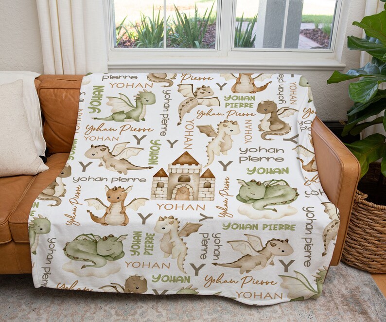 May include: White fleece blanket with a repeating pattern of green and brown dragons, a castle, and the names "Yohan" and "Pierre".