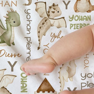 Peut inclure: Une couverture de bébé blanche avec un motif de dragon brun et vert. La couverture présente les noms "Yohan Pierre" et "Yohan" répétés tout au long du motif. La couverture est faite d'un tissu doux et confortable et est parfaite pour la chambre d'un bébé.