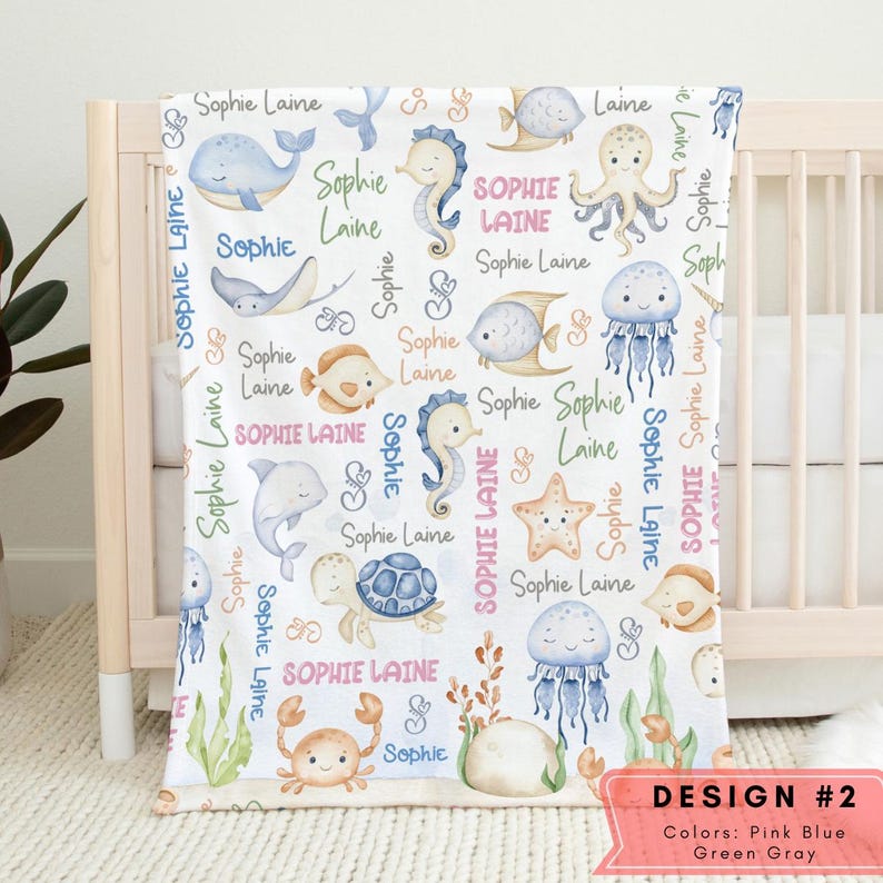 May include: A white baby blanket with a sea life pattern. The blanket features a variety of sea creatures, including a whale, a seahorse, an octopus, a jellyfish, a starfish, a turtle, and a crab. The blanket is decorated with the name "Sophie Laine" repeated throughout. The blanket is designed in pink, blue, green, and gray.
