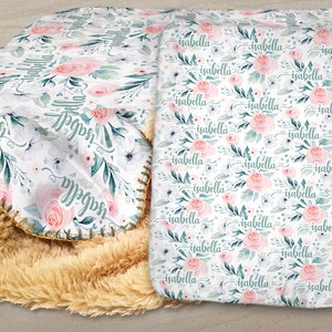 May include: A white fleece blanket with a floral pattern and the name "Isabella" repeated throughout. The blanket has a light brown sherpa backing.