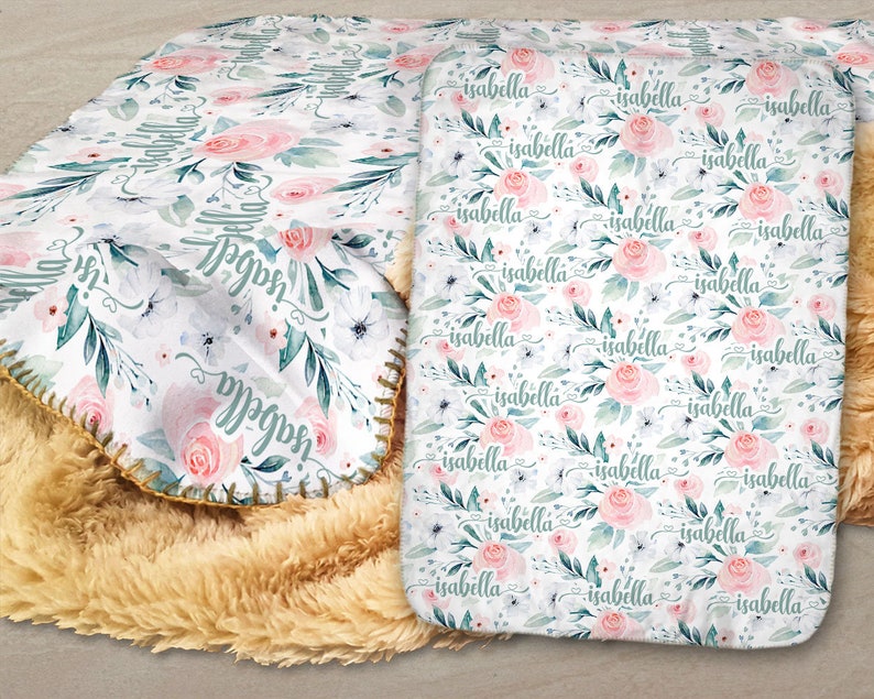 May include: A white fleece blanket with a floral pattern and the name "Isabella" repeated throughout. The blanket has a light brown sherpa backing.