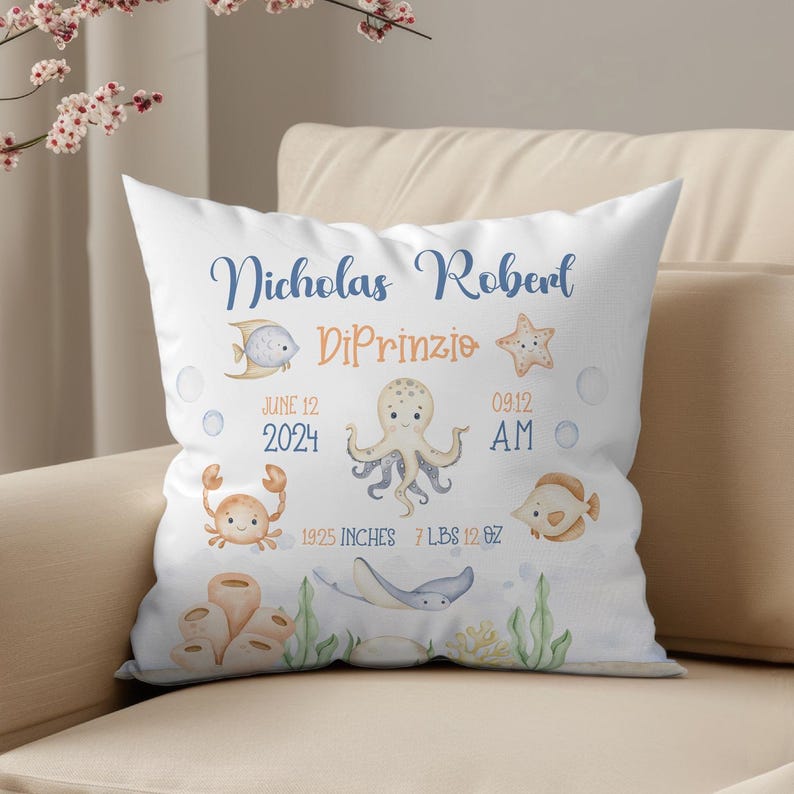 May include: A white pillow with a blue and orange ocean-themed design. It says "Nicholas Robert DiPrinzio" with the birth date "June 12, 2024" and time "09:12 AM". It also says "19.25 inches, 7 lbs 12 oz".