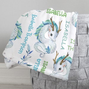 May include: White baby blanket with a repeating pattern of blue and green watercolor dragons. The blanket has the name "Isabella Thompson" written on it.